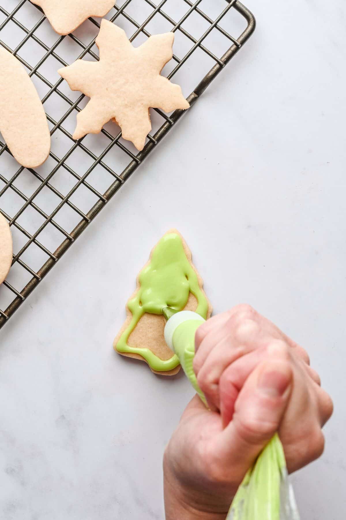 Green icing in a pastry bag being added to a cutout Christmas tree cookie.