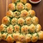 Christmas tree pull apart bread on a cutting board with marinara sauce on the side.