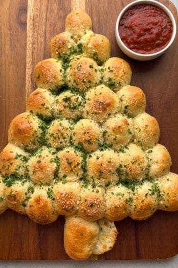 Christmas tree pull apart bread on a cutting board with marinara sauce on the side.