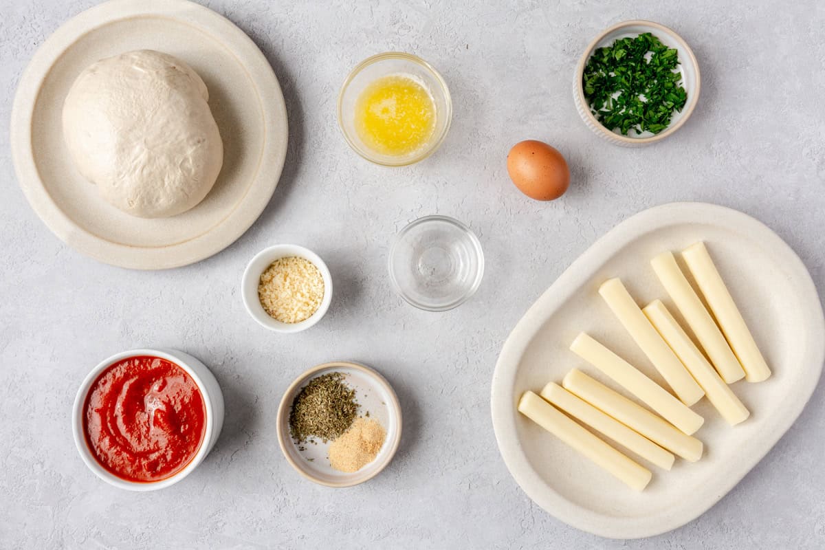 Ingredients for recipe: pizza dough, melted butter, cheese stick, grated parmesan, fresh parsley, seasonings, and marinara sauce.