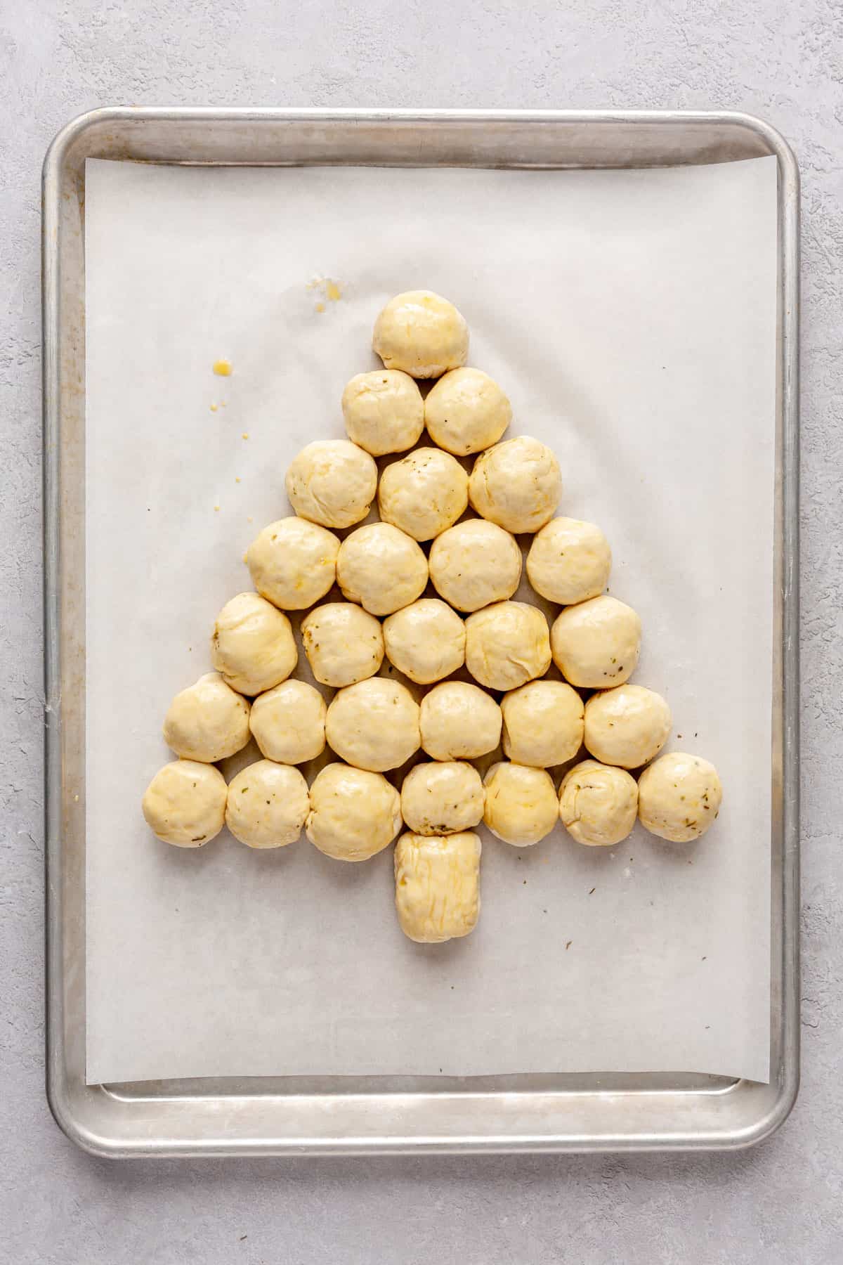 Cheese stuffed dough balls on a baking sheet seam side down in the shape of a tree after brushing with egg wash, before baking.