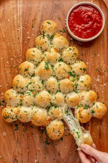 Christmas tree pull apart bread on board with hand pulling a piece with a cheese pull.