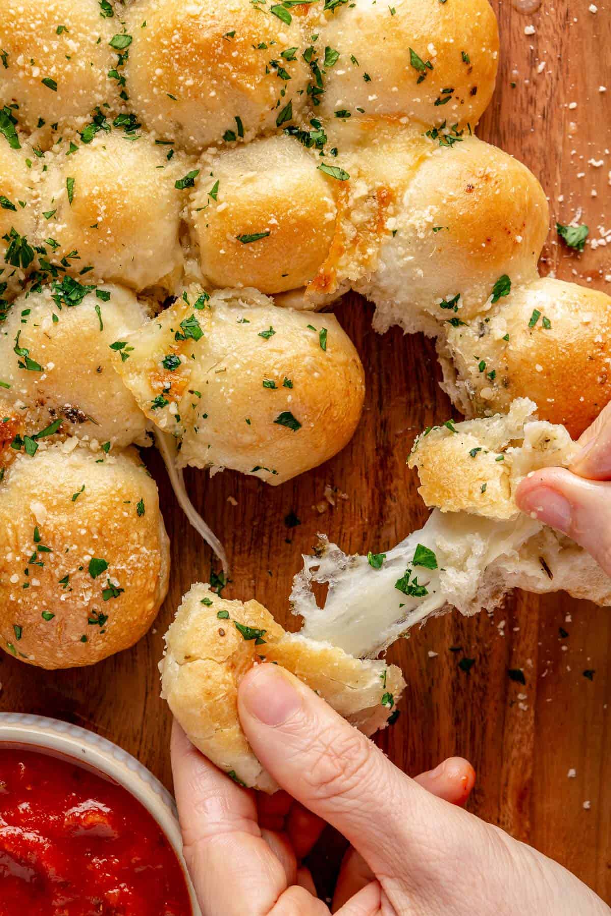 Hands pulling a cheese bread apart with cheese stretching across.