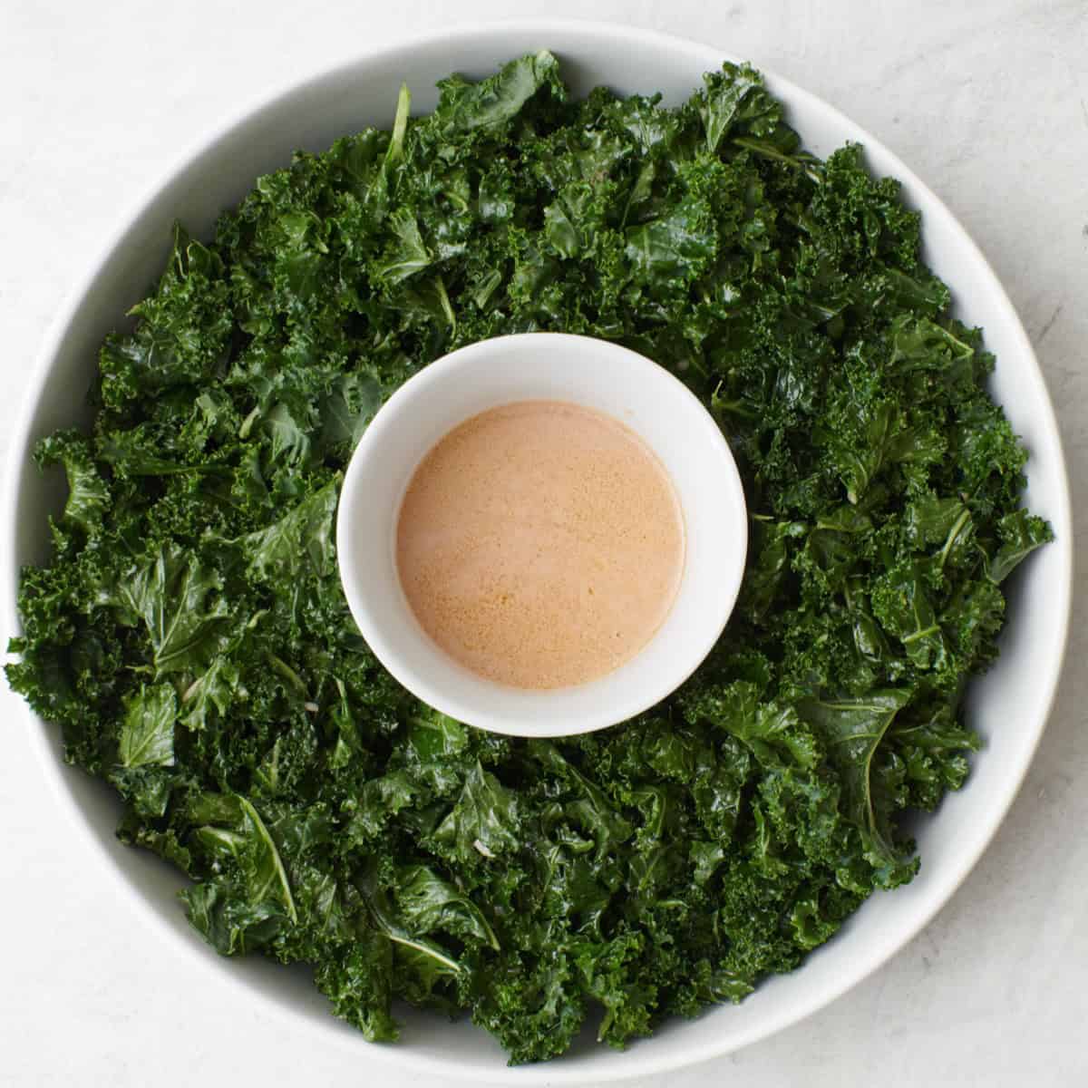 Dressed kale added to platter with dressing in the center.