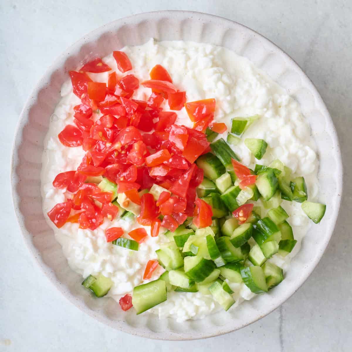 Chopped tomatoes and cucumbers added on top of bowl.