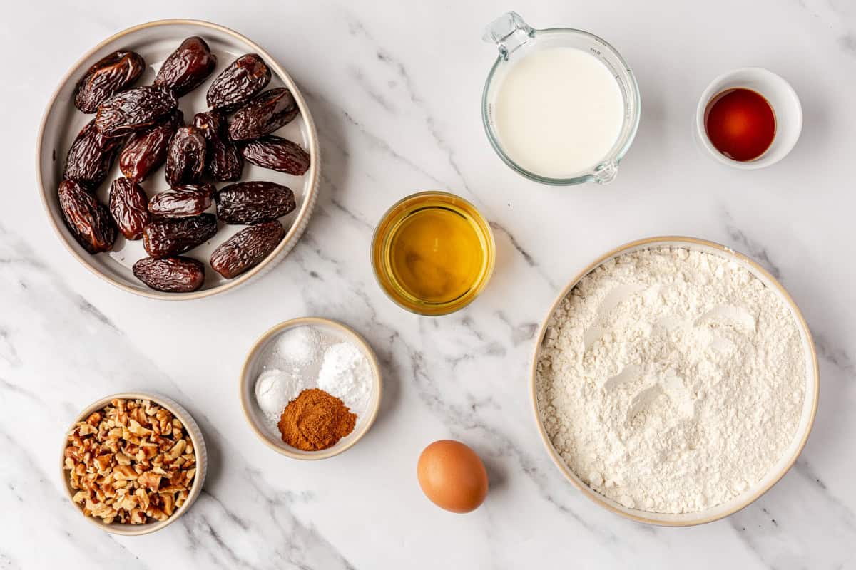 Ingredients for recipe before prepping: dates, walnuts, cinnamon, baking powder, baking soda, salt, oil, milk, egg, flour, and vanilla.