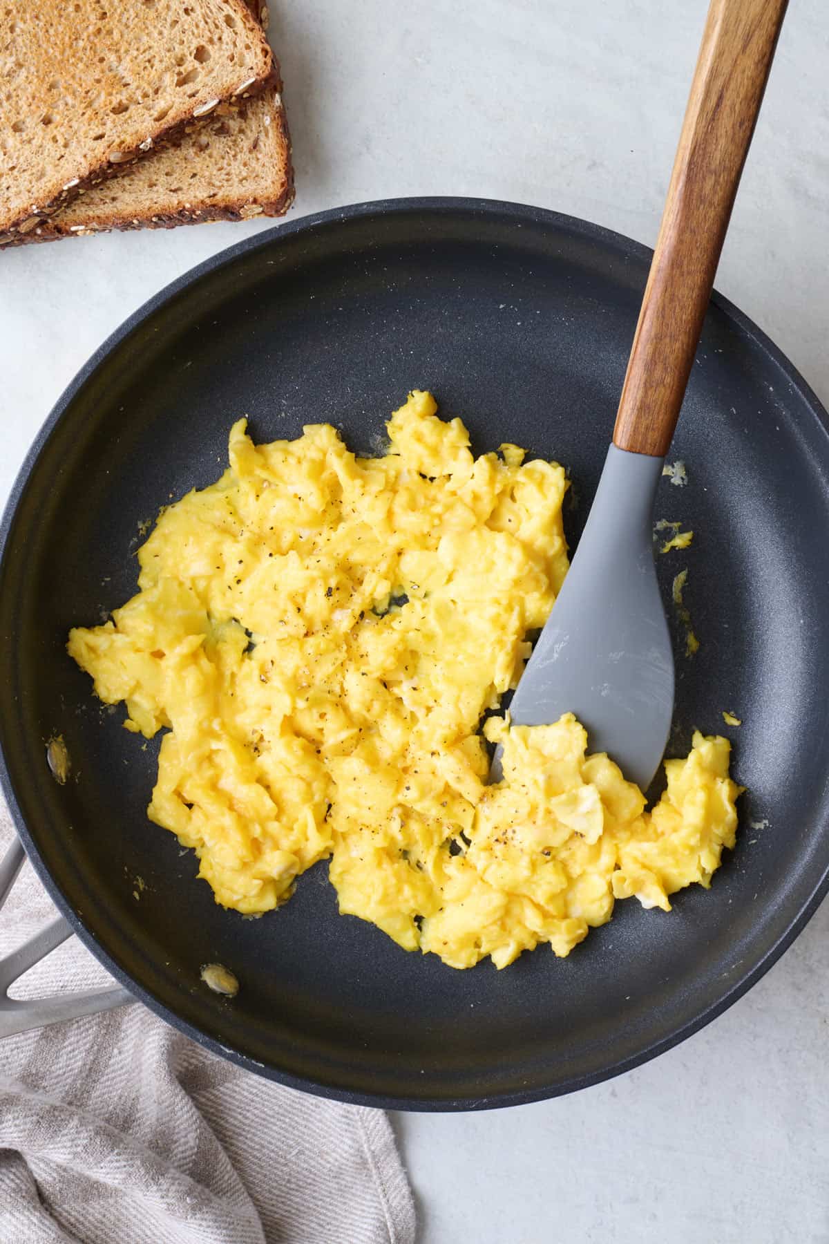 Homemade fluffy scrambled eggs in small skillet with rubber spatula slightly under them