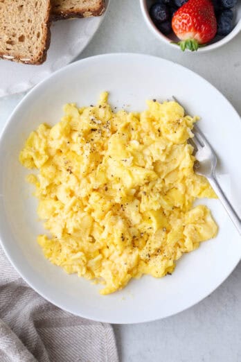 Serving of scrambled eggs on a plate with a fork.