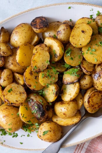 Platter with grilled potatoes garnished with parsley and spoon on side.