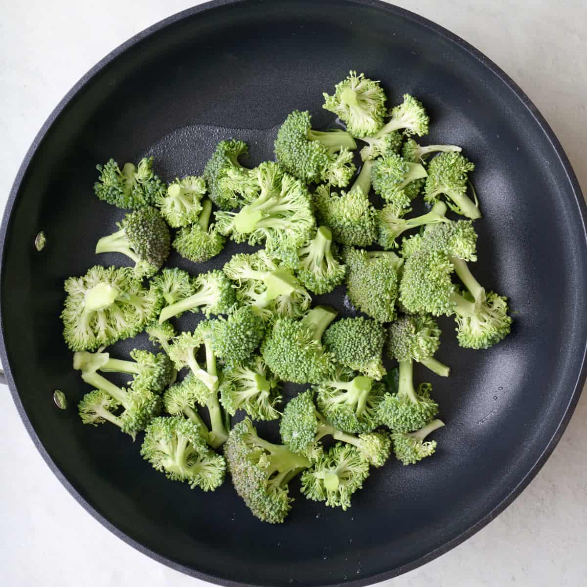 Uncooked broccoli florets in a skillet.