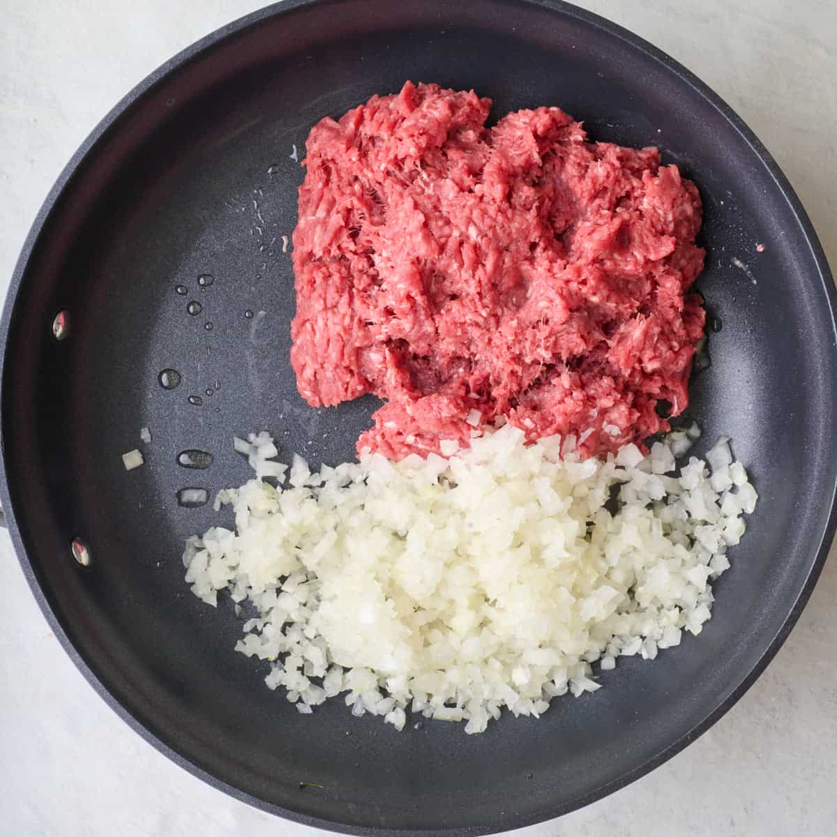 Ground beef and onions in an oiled skillet before cookiing.