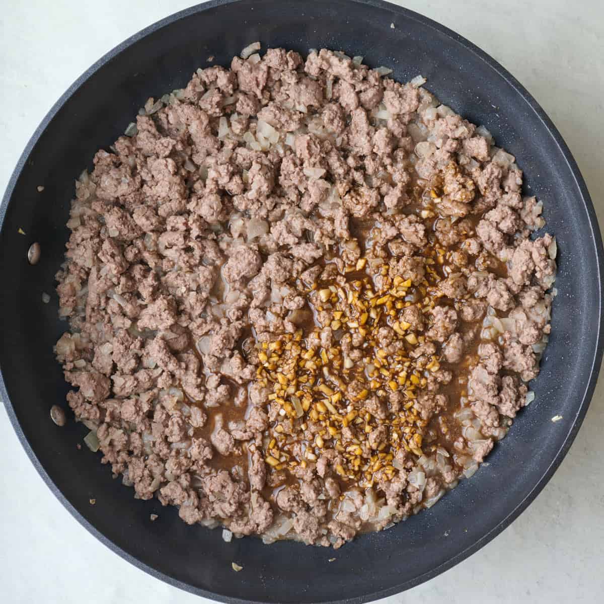 Cooked ground beef with onions in a skillet with marinade added.