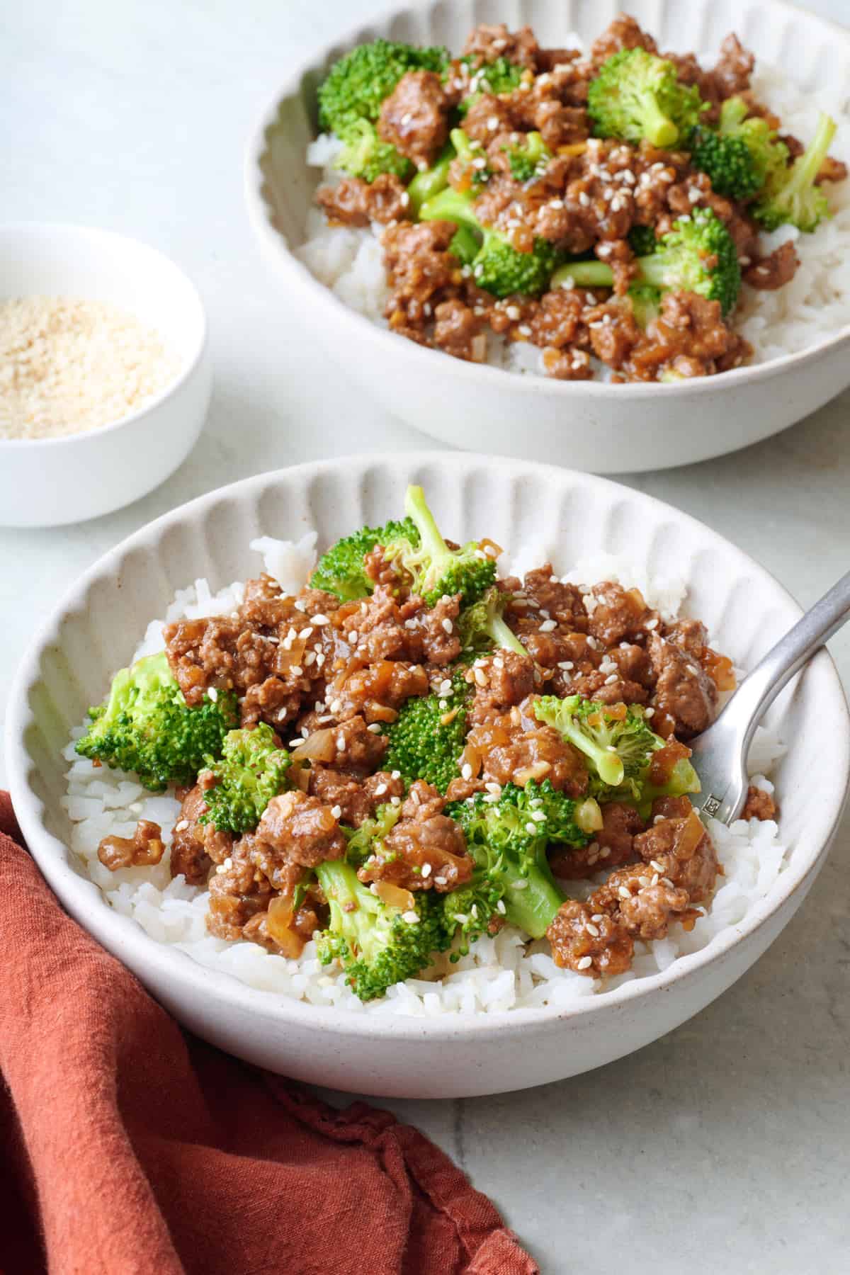 Two servings of easy ground beef & broccoli served over white rice and a fork dipped inside bowl.