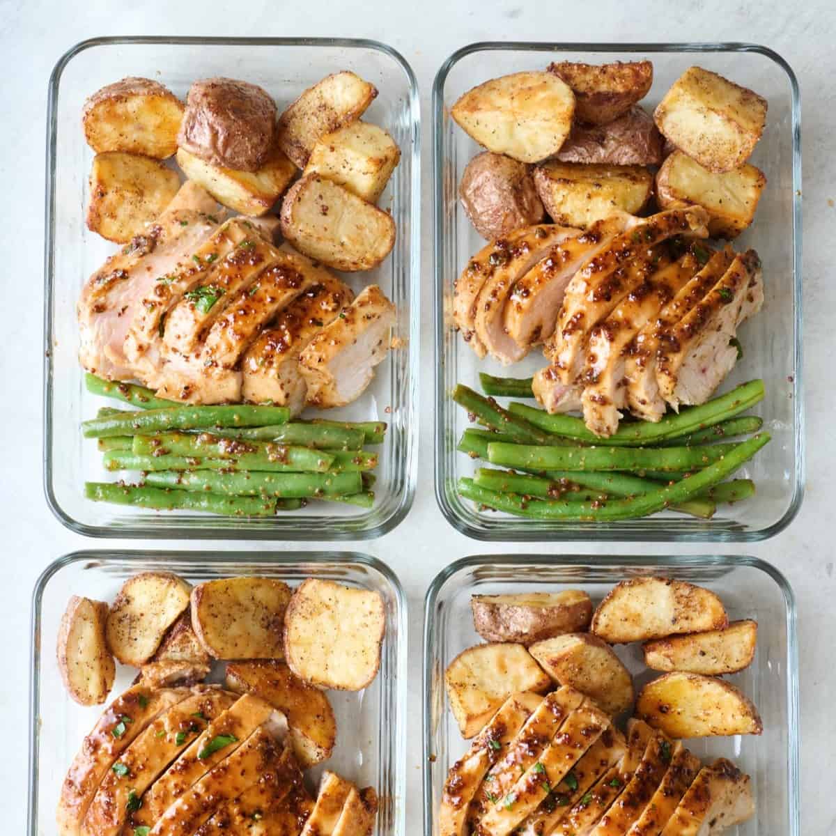 Honey mustard chicken with roasted potatoes and green beans in meal prep containers.