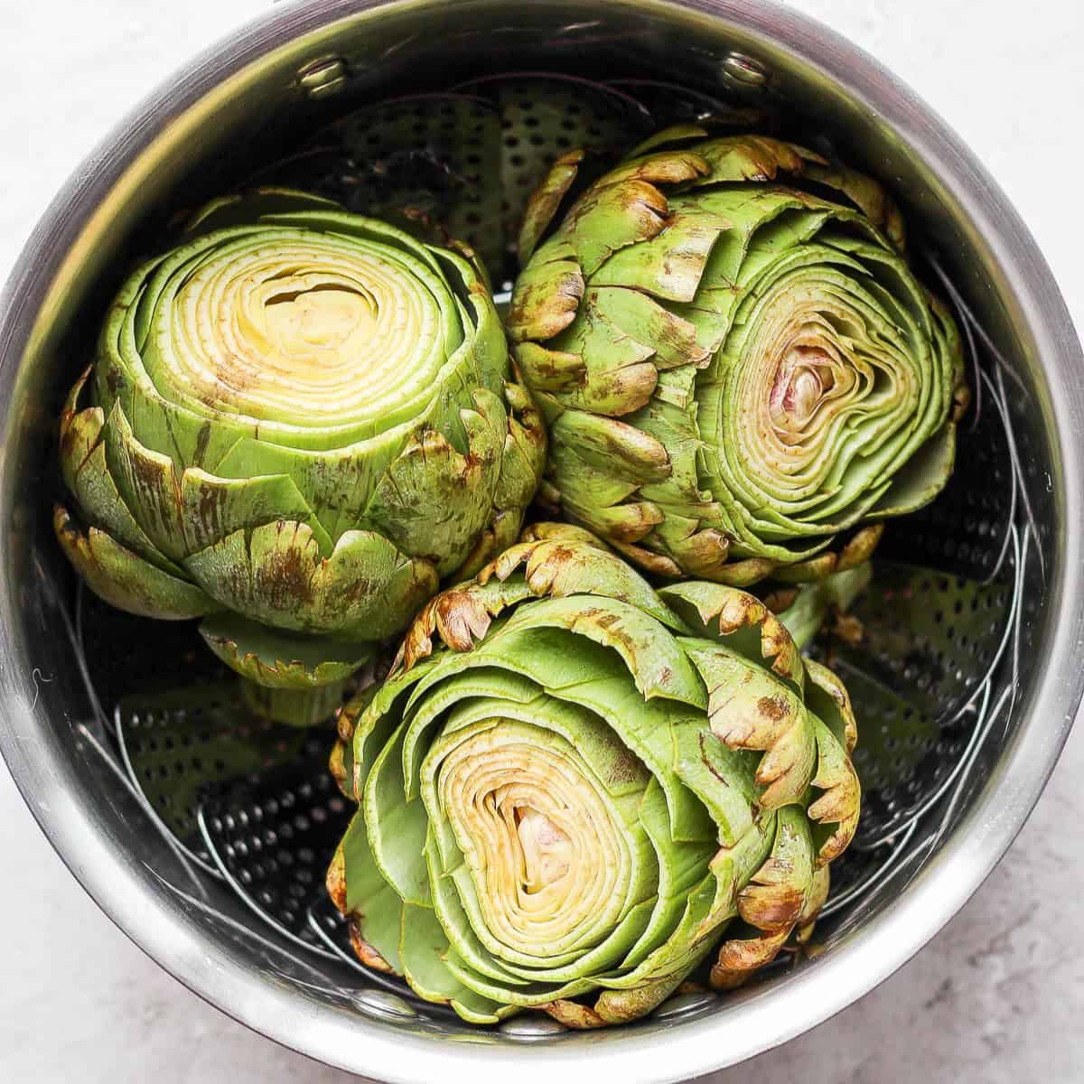 Prepared artichokes in a steamer basket.