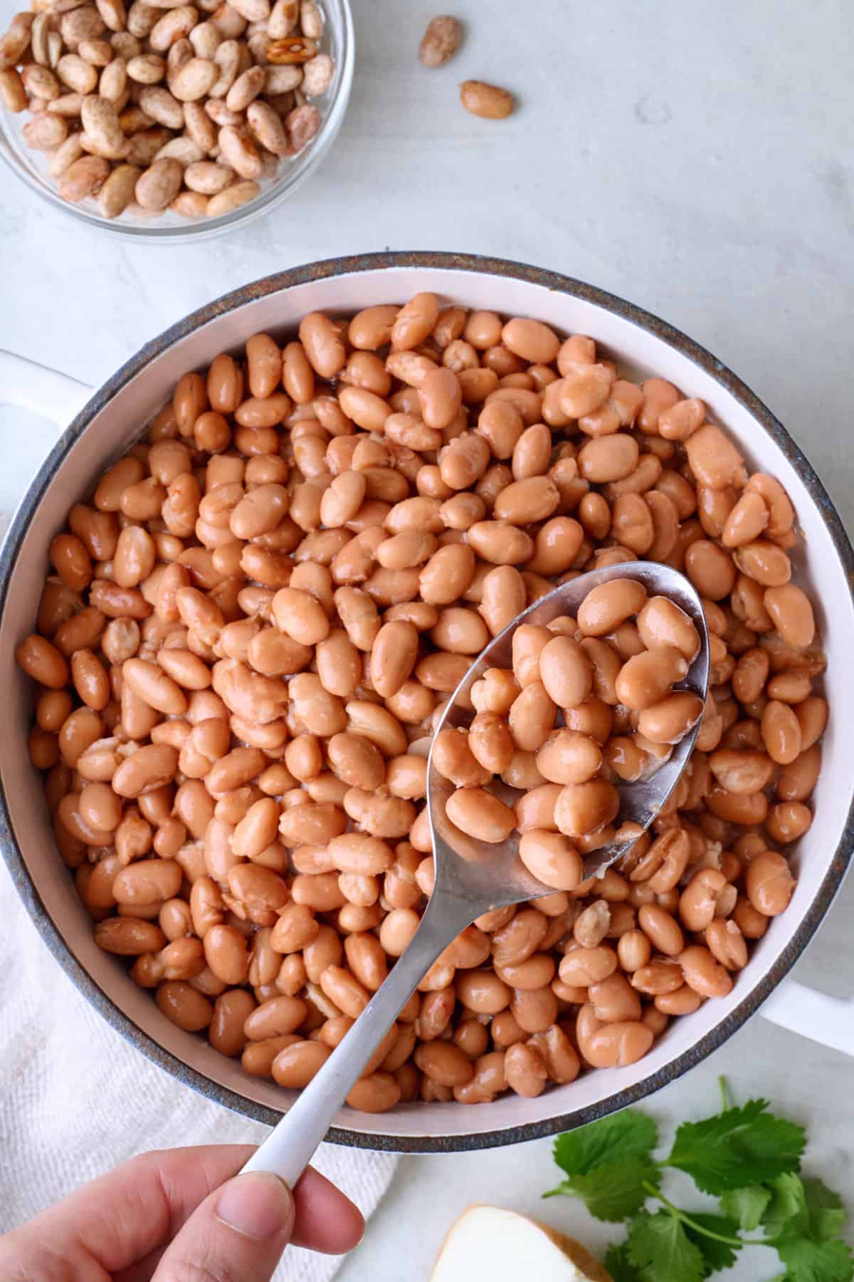 Spoon lifting up cooked pinto beans from pot.