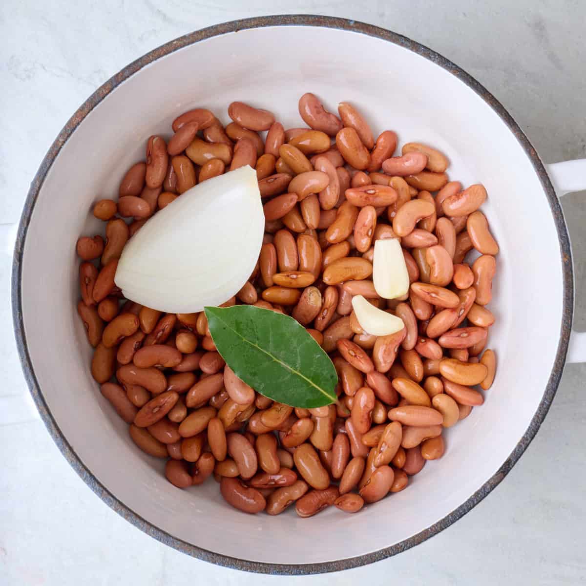 Soaked kidney beans in a pot with onion, garlic, and a bay leaf.