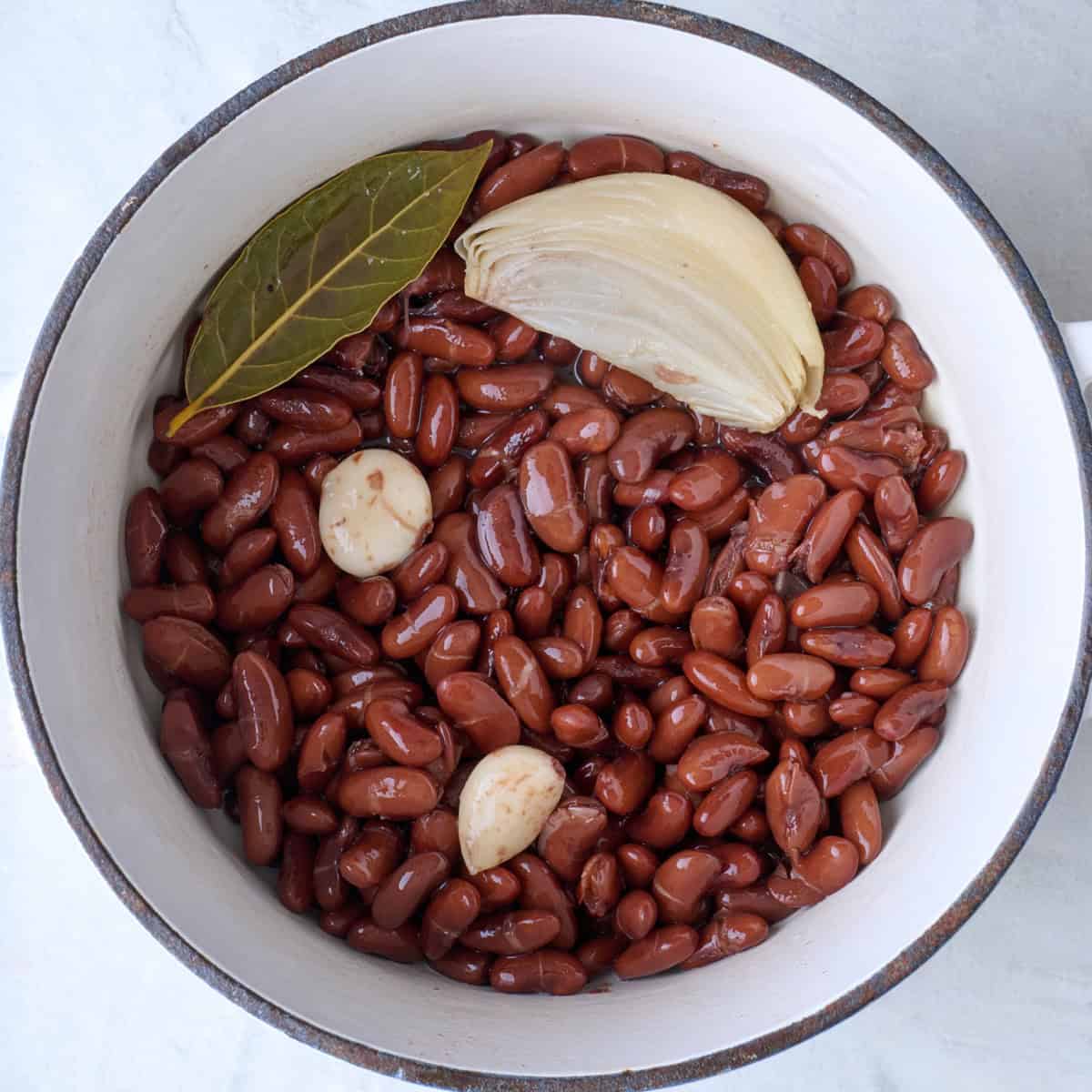 Cooked and drained kidney beans in a pot with aromatics.