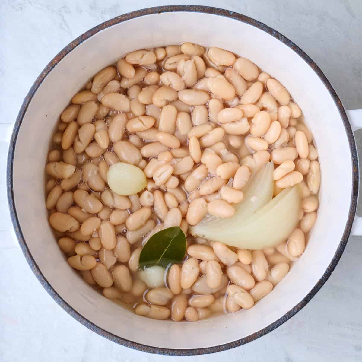 Cooked cannellini beans in a pot with aromatics.