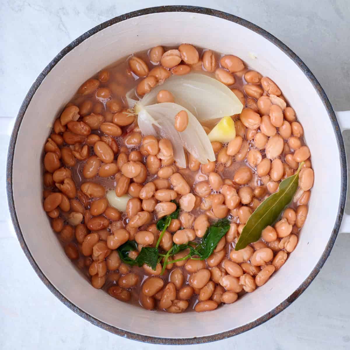 Cooked pinto beans in a pot with aromatics.