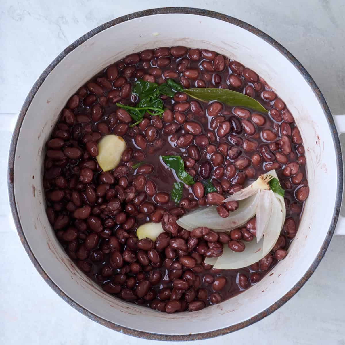 Cooked black beans in a pot with aromatics.