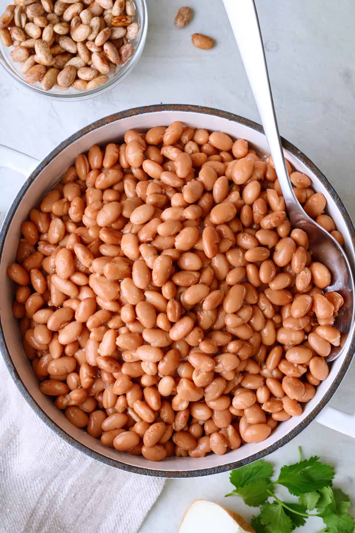 Cooked pinto beans in a pot with spoon dipped inside.