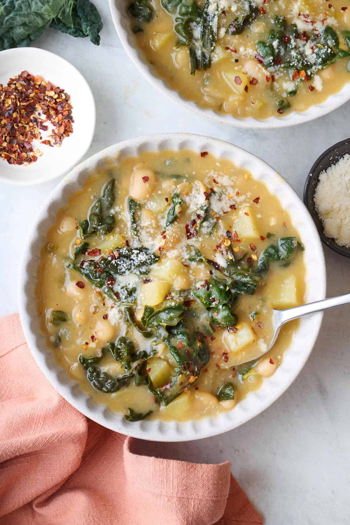 Bowl of kale soup with beans and potatoes with a spoon dipped inside.