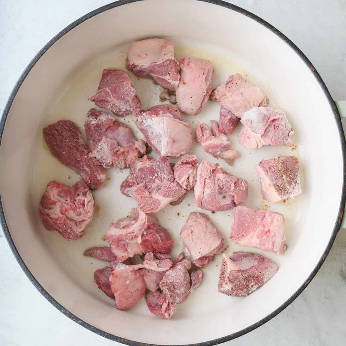 Half of the floured lamb pieces in an oiled pot.