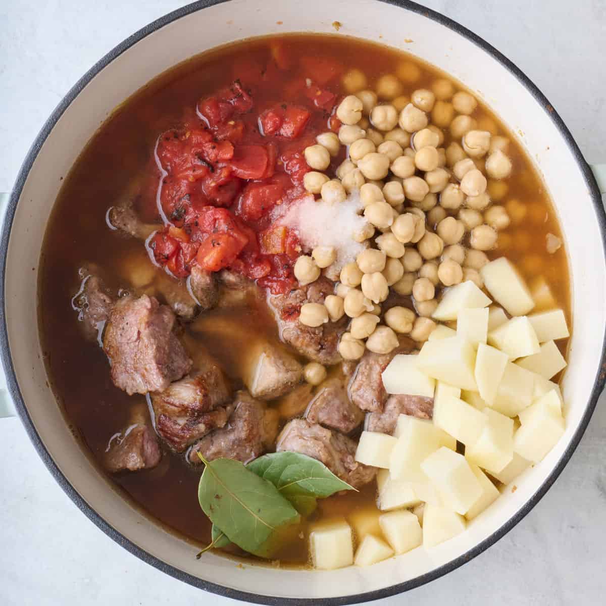 Broth, tomatoes, chickpeas, potatoes, bay leaves, salt and pepper added to pot.