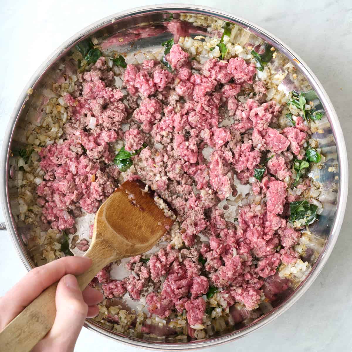 Ground beef added with spatula breaking partially cooked into smaller pieces.