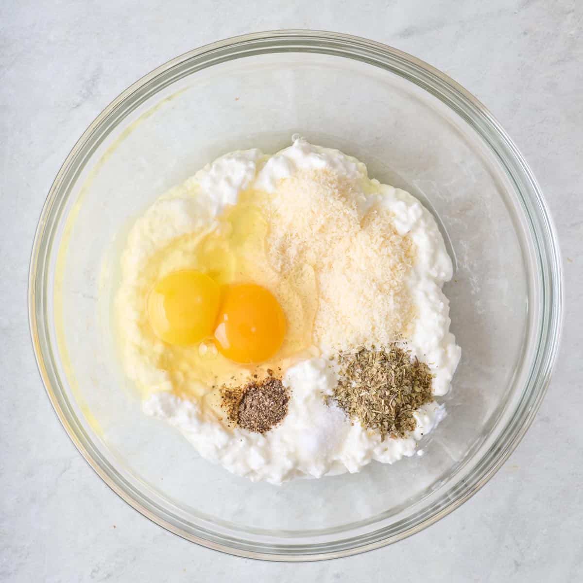 Cottage cheese, parmesan, egg and seasoning in a bowl before combining.