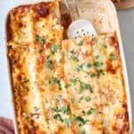 Lasagna made with cottage cheese and meat sauce in a baking dish after cutting with a large serving removed to a plate nearby.