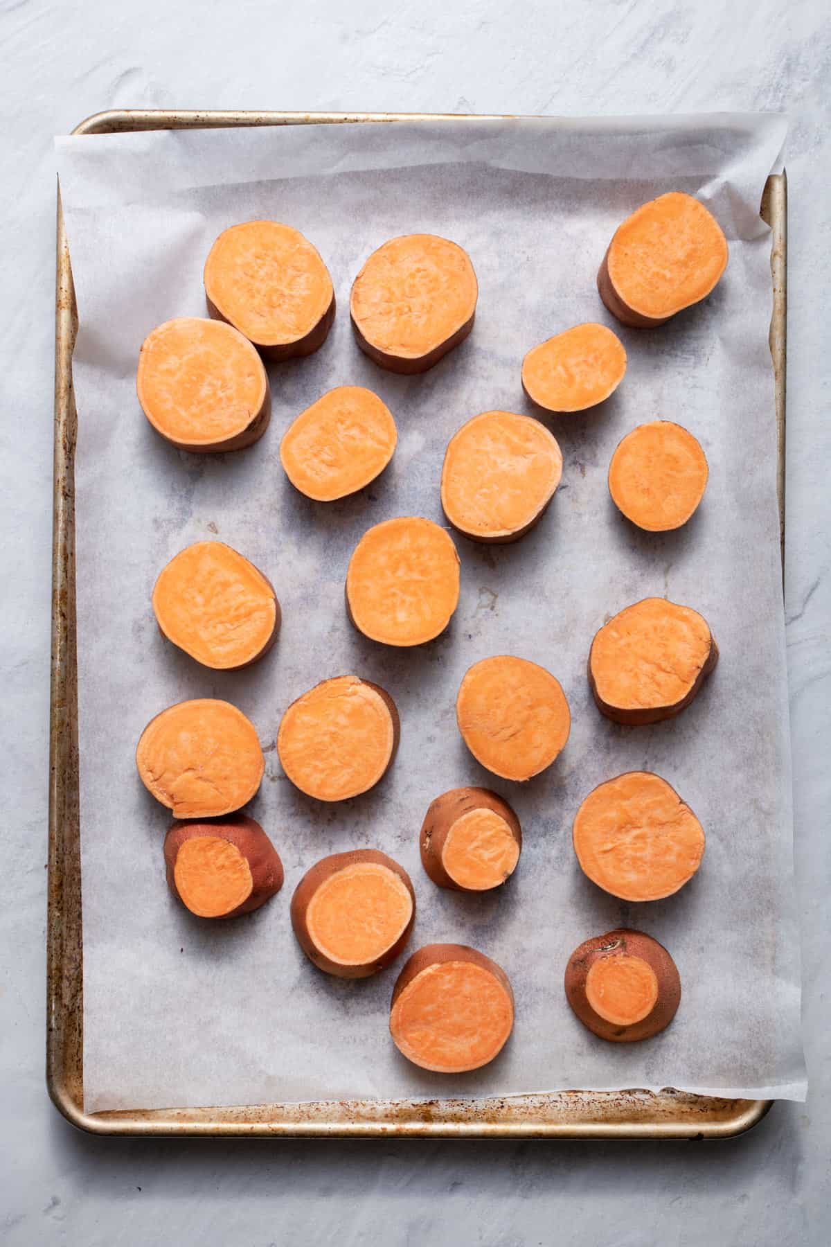 Sweet potato rounds on a sheet of parchment paper on baking tray.