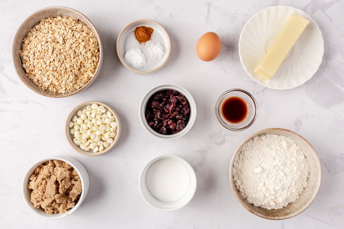 Ingredients for recipe: oats, white chocolate chips, brown sugar, cinnamon, salt, dried cranberries, sugar, an egg, vanilla extract, butter, and flour.