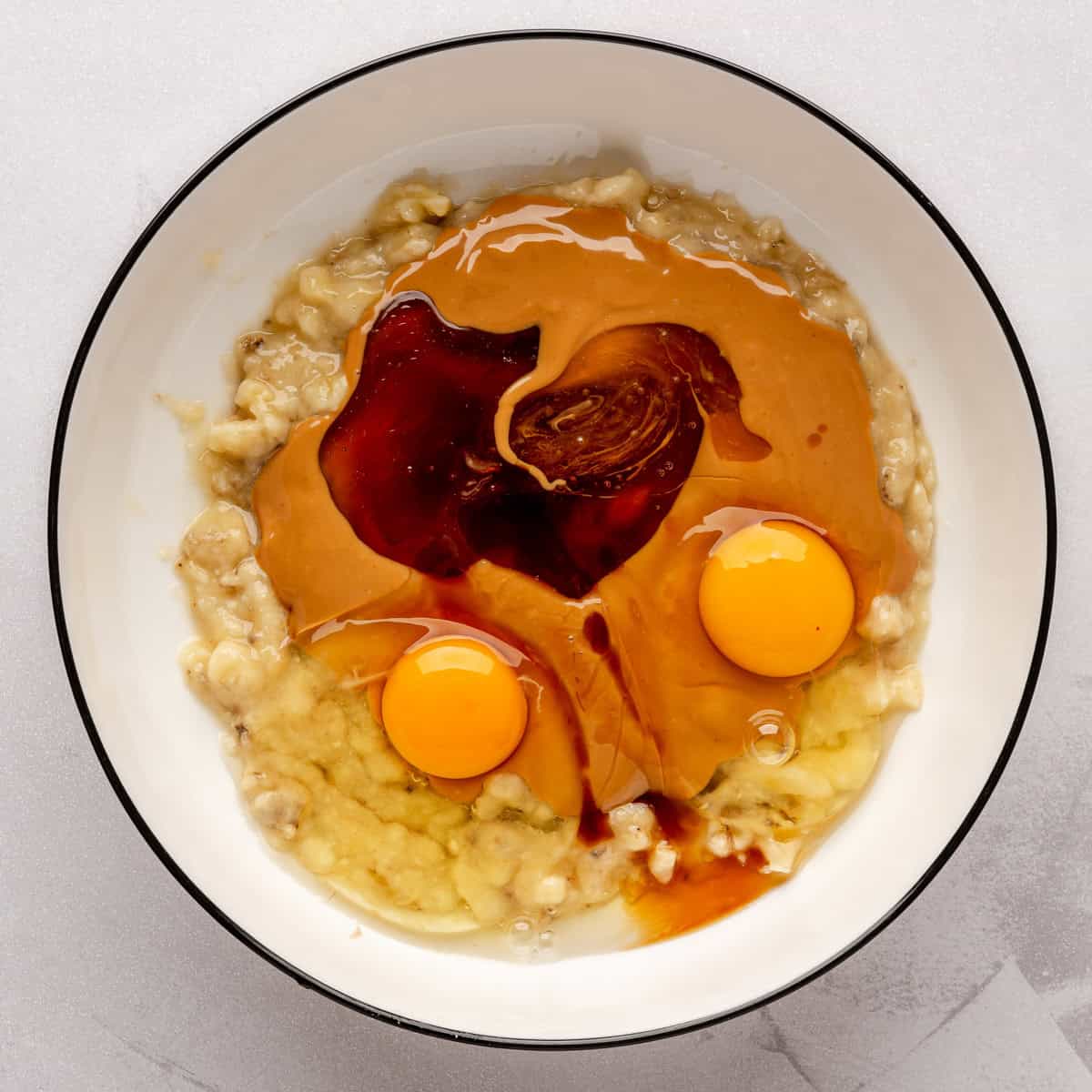 Mashed bananas, eggs, honey, and vanilla in a bowl.