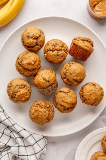 Peanut Butter Banana Muffins on a round platter with small jar of peanut butter and banana nearby.