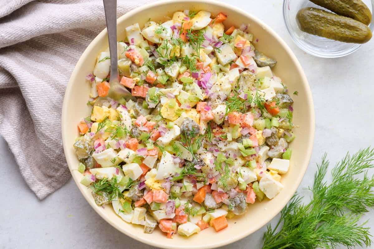 Crunch pickle salad in a serving bowl with fresh dill and dill pickles nearby.