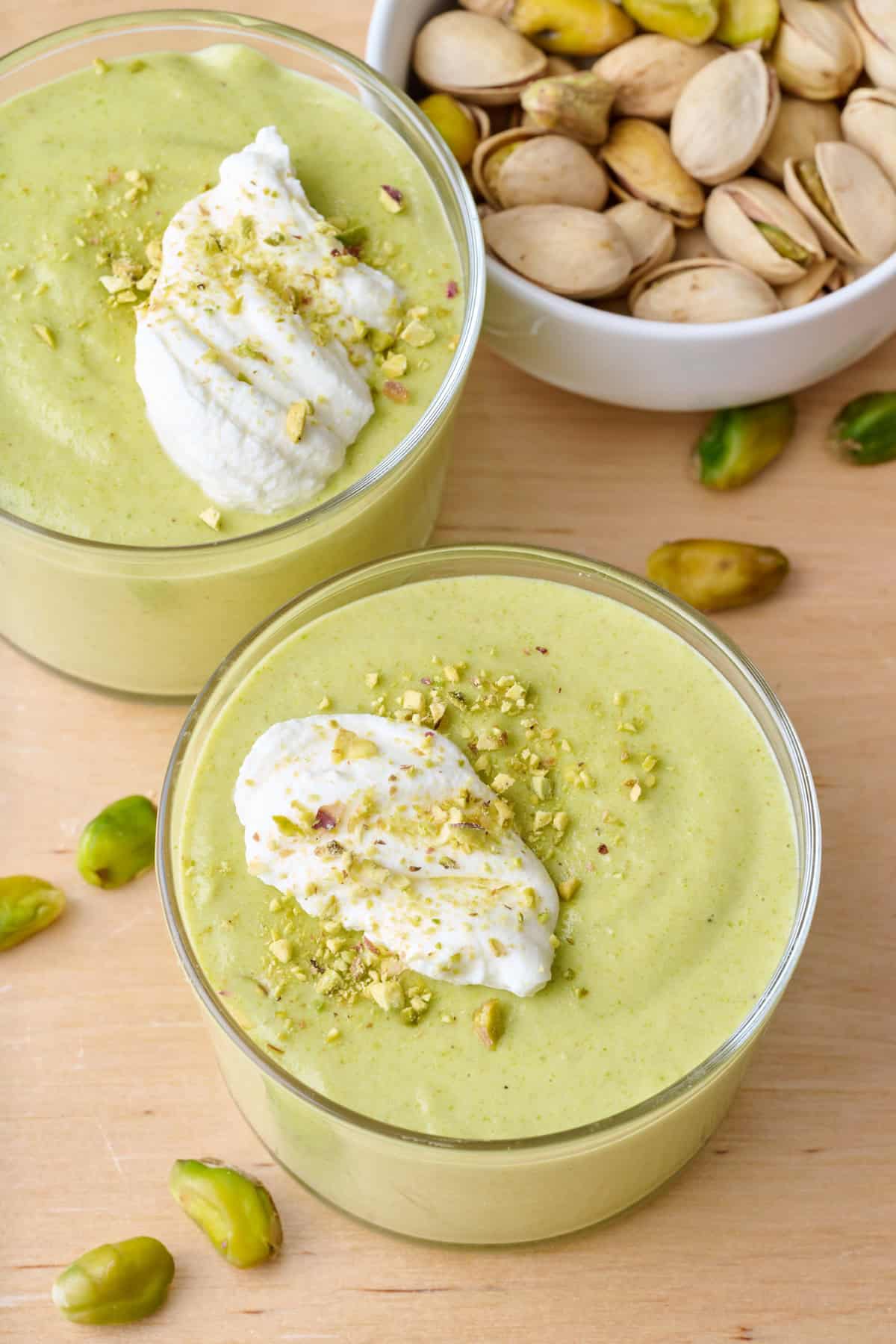 Homemade pistachio pudding in two serving glasses topped with whipped cream and extra crushed pistachios.