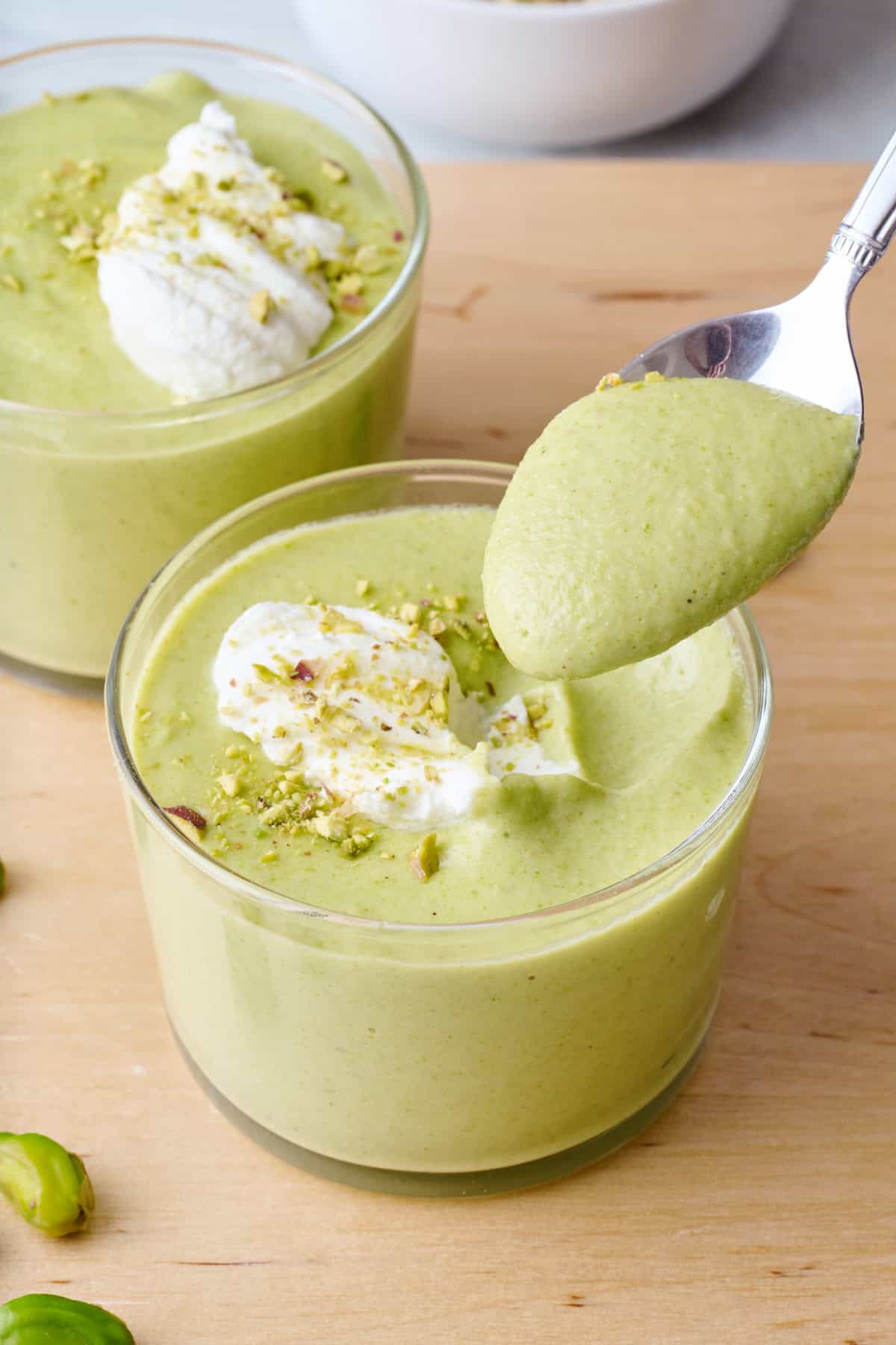 Homemade pistachio pudding in two serving glasses with a spoon lifting up a bite.