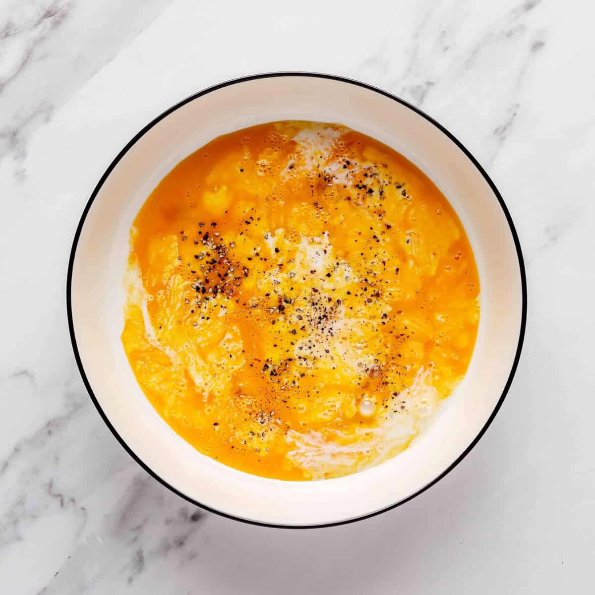 Eggs, milk, yogurt, salt and pepper in a bowl before whisking.