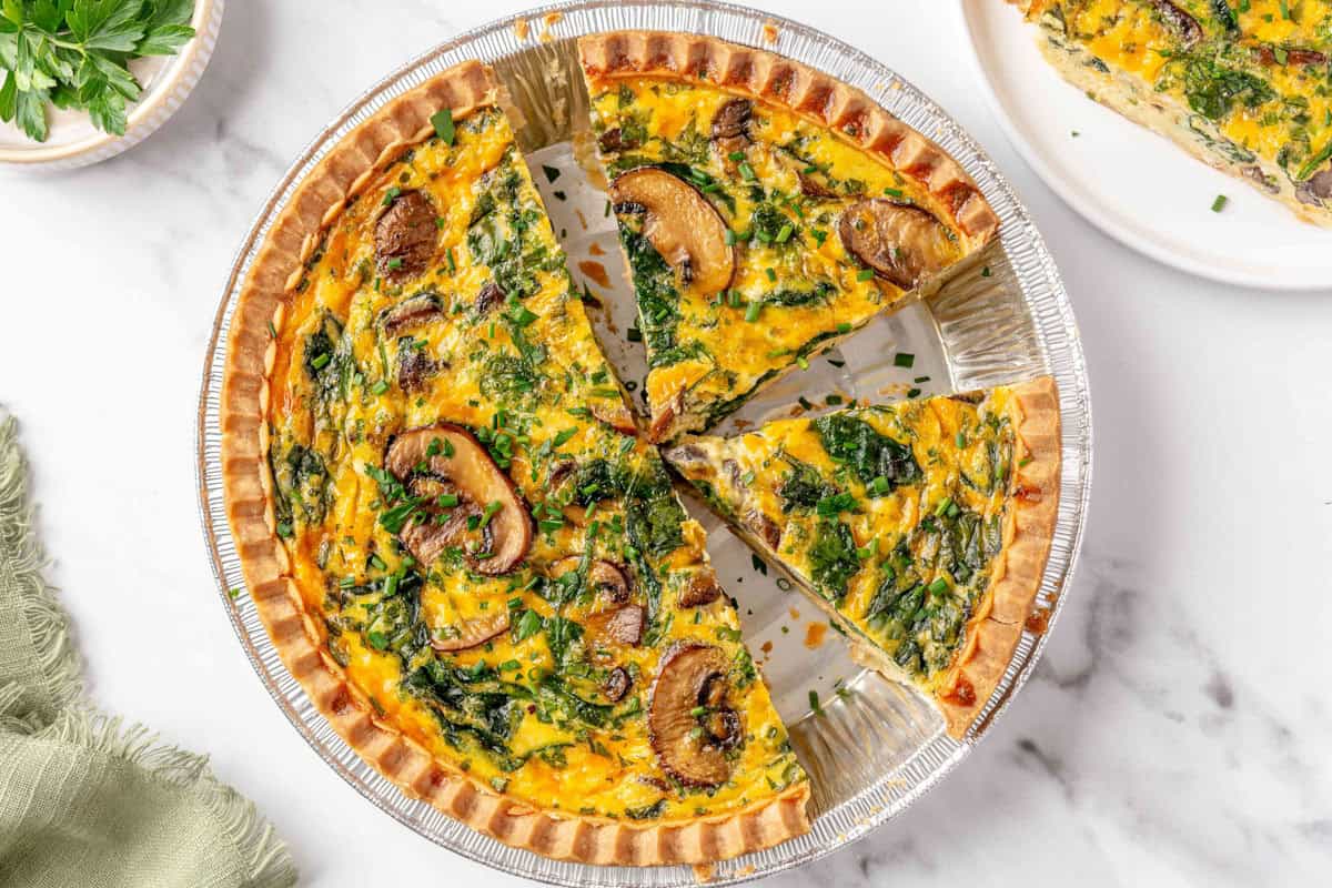 Quiche in a pie dish with one slice being taken out.