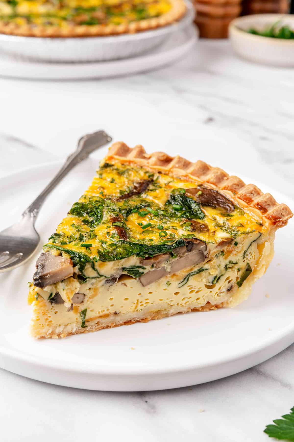 Slice of quiche on a plate showing the filling and layers of toppings throughout.