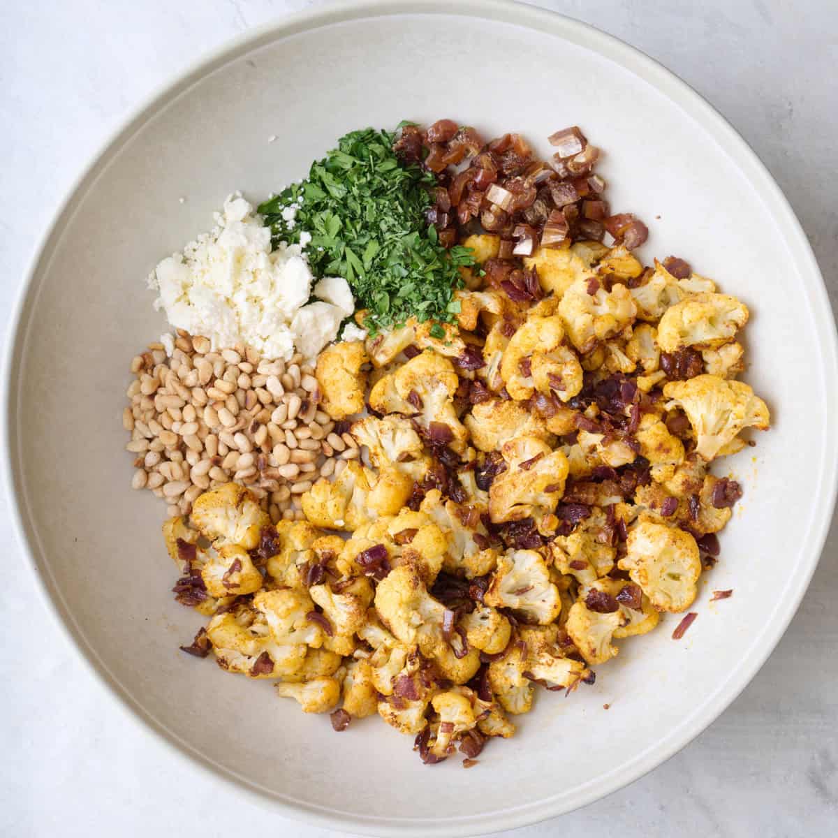 Roasted cauliflower, dates, parsley, feta and nuts layered in a wide shallow bowl or serving platter.