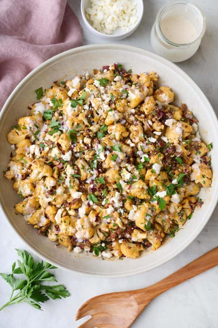 Roasted cauliflower salad on a platter garnished with extra feta and parsley and dressing nearby.