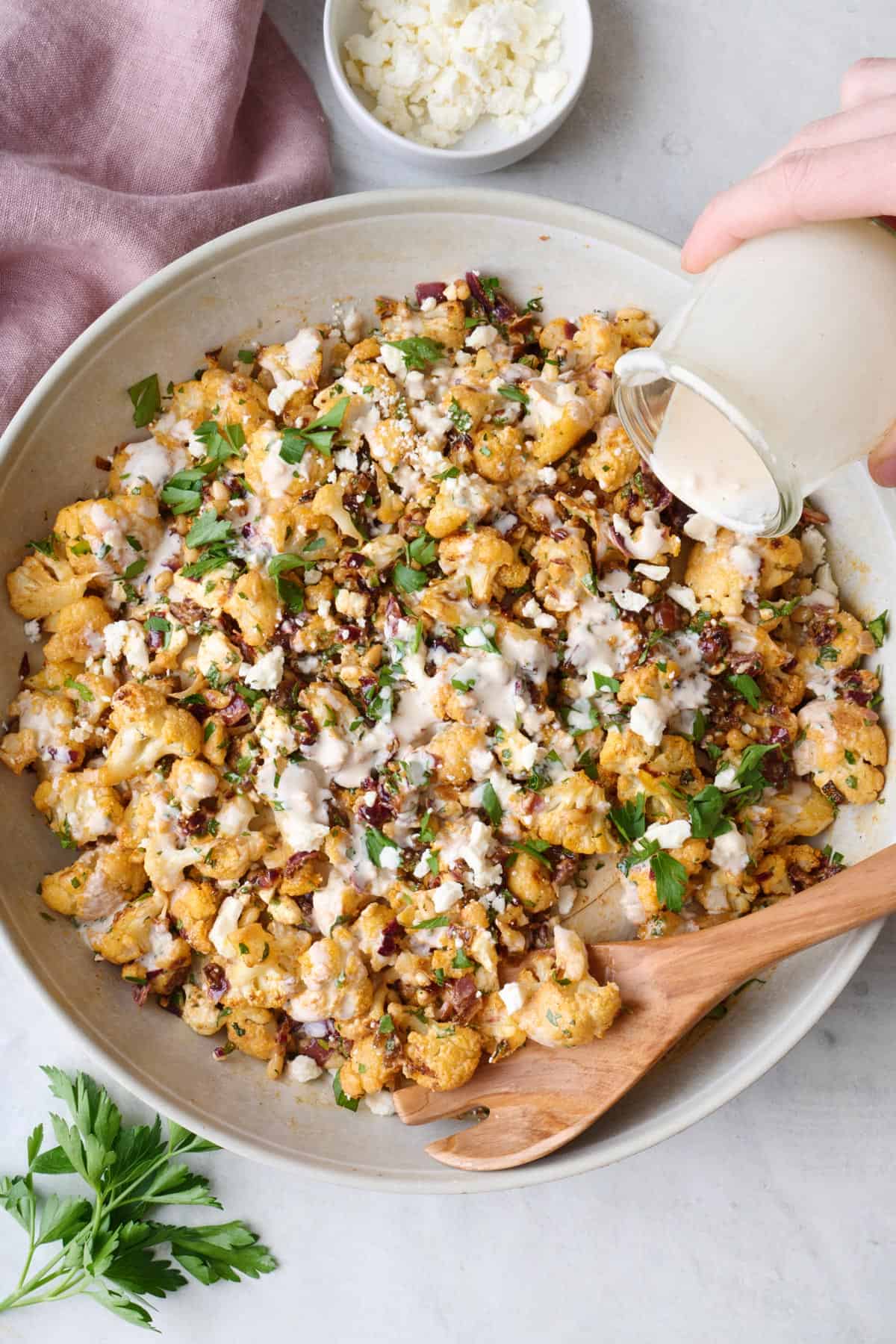 Roasted cauliflower and onion salad in a large serving bowl with tahini dressing being poured over.