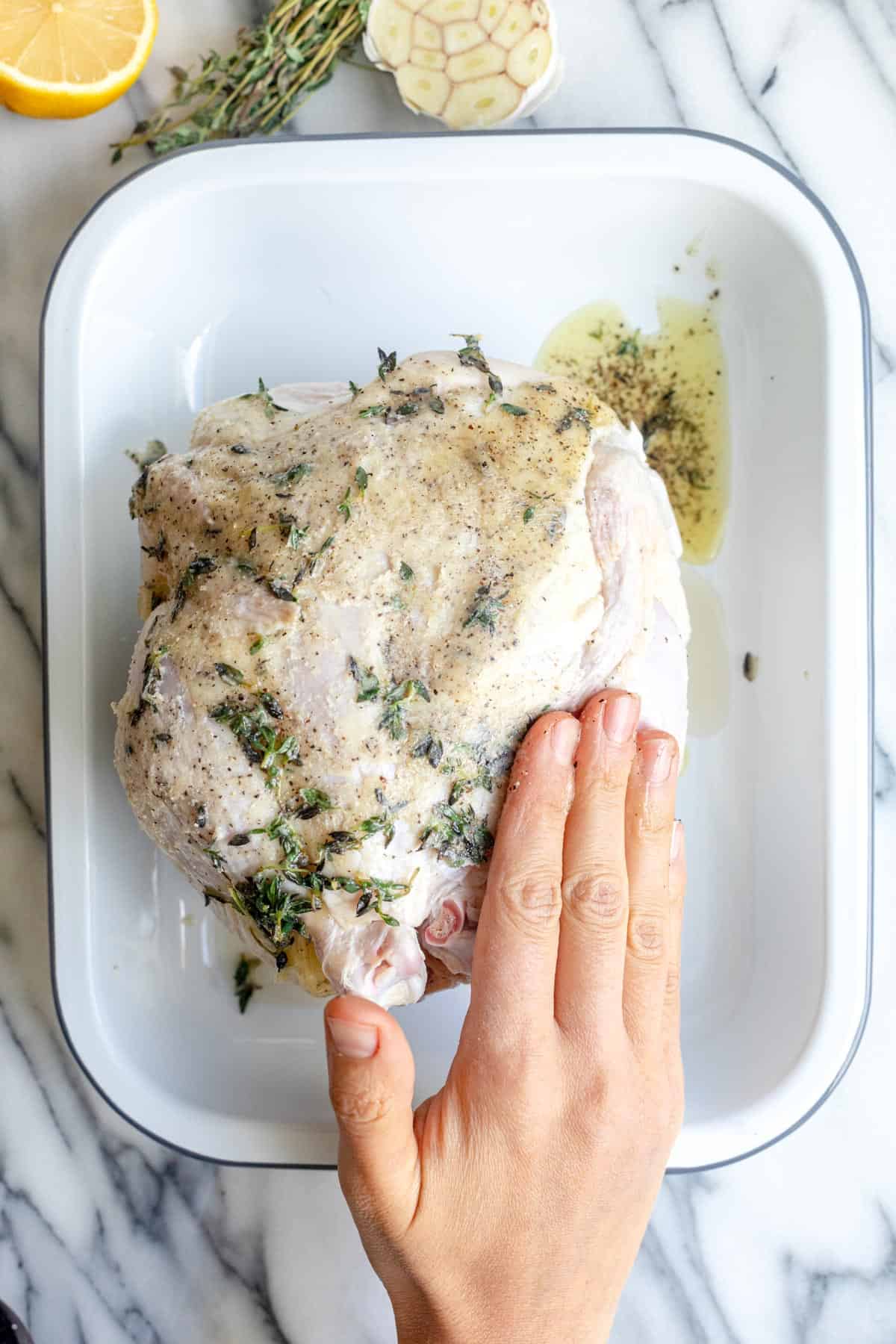 Rubbing oil and seasoning onto the skin of chicken.