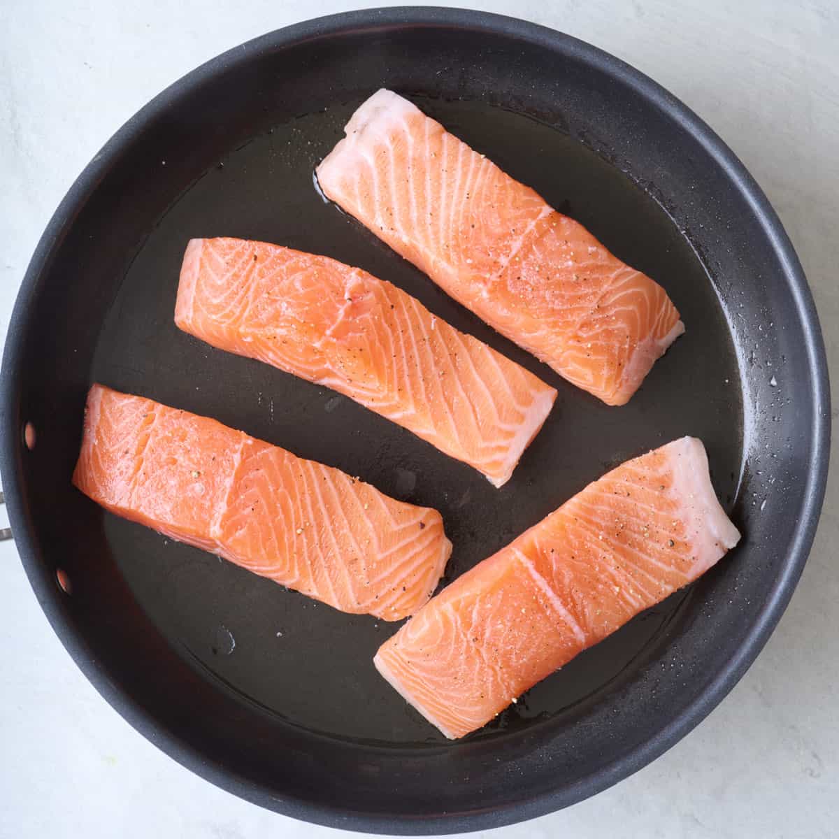 Salmon fillets skin side down on skillet seasoned with salt and pepper.