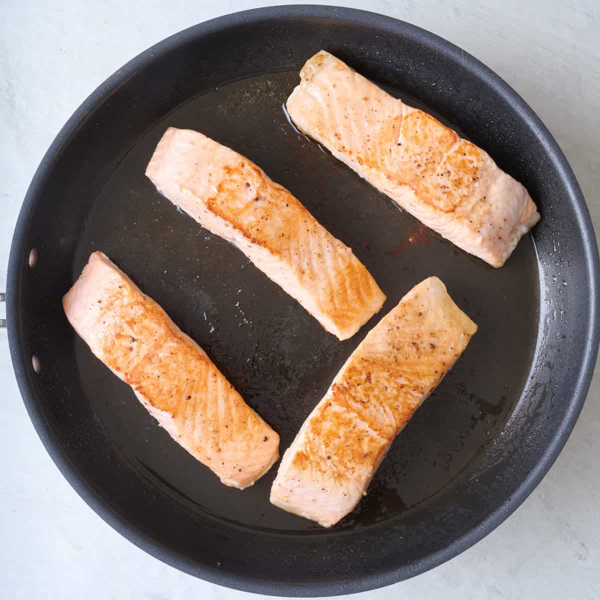 Salmon fillets skin side down on skillet after cooked.