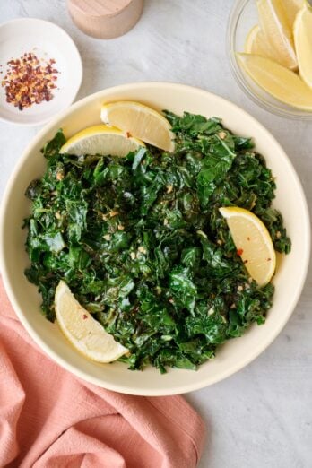 Sauteed kale in a shallow serving bowl with lemon wedges and small dish of extra lemons nearby.