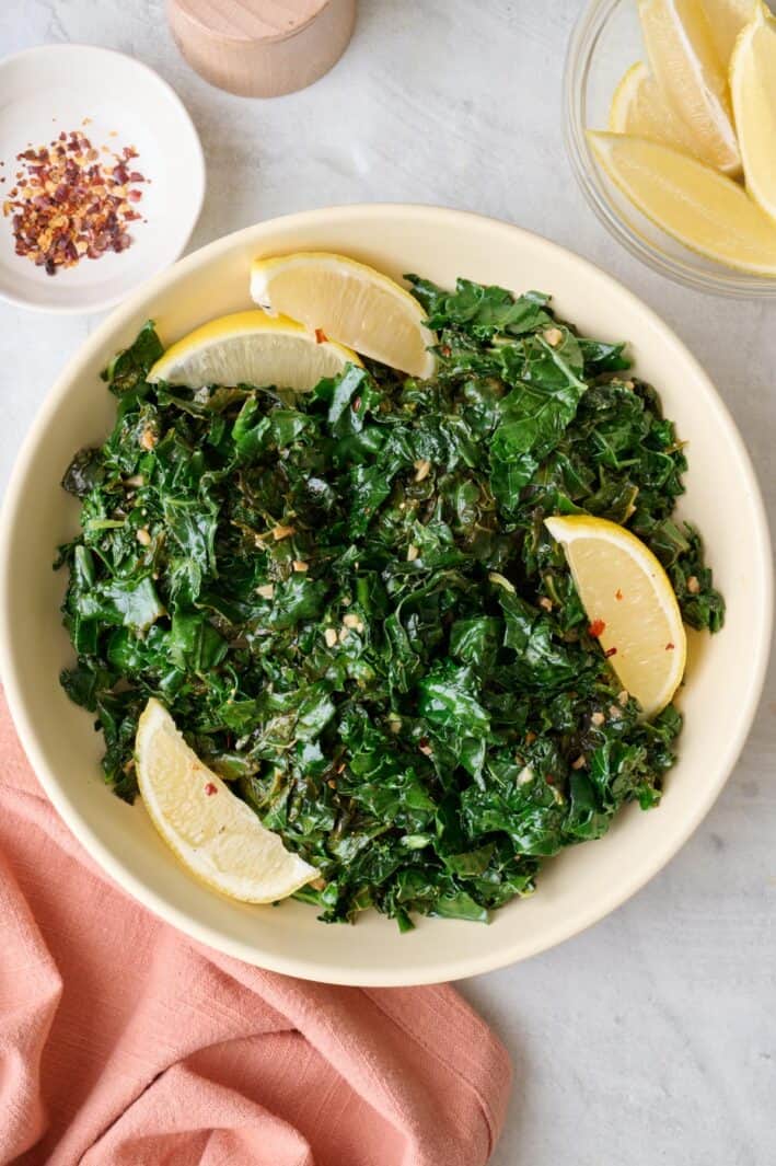 Sauteed kale in a shallow serving bowl with lemon wedges and small dish of extra lemons nearby.